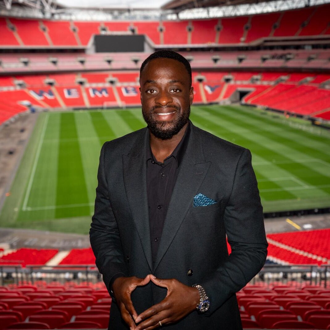 A man in suit and tie standing in front of an empty stadium.