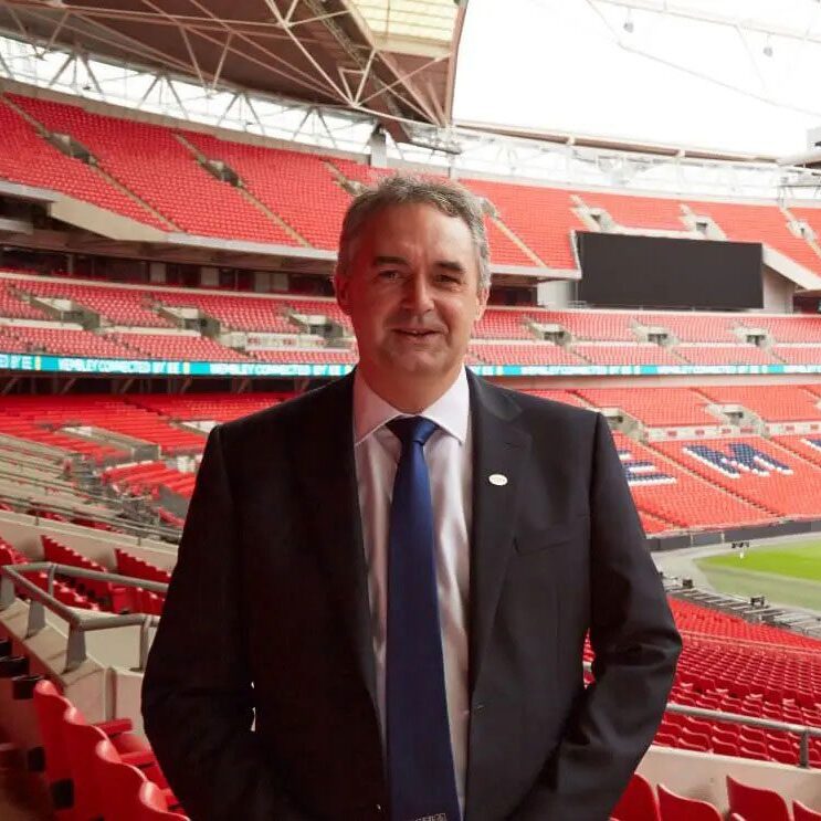 A man in suit and tie standing in front of an empty stadium.